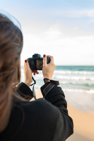 Smiling female photographer holding a camera on a sunny beach, enjoying golden hour light and capturing outdoor moments on the coastline.の写真素材