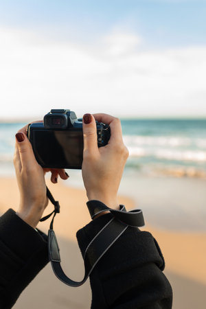 Close-up of woman holding a professional camera on the beach during golden hour, focusing on the lens and capturing outdoor photography moments.の写真素材