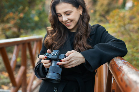 Close-up of a young woman holding a digital camera while photographing outdoors in warm sunlight....