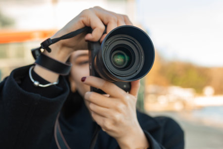 Low-angle view of a female photographer holding a camera against the blue sky, capturing outdoor...