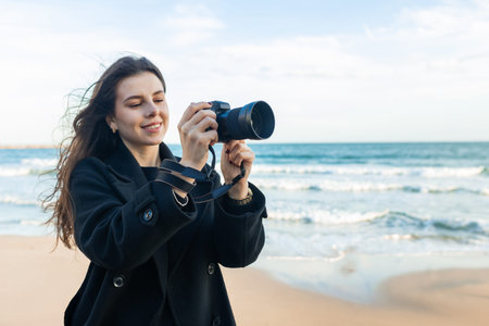 Smiling female photographer holding a camera on a sunny beach, enjoying golden hour light and...
