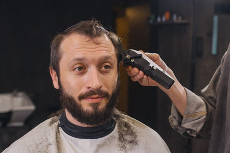 Professional barber trimming client hair with electric clipper in modern barbershop. Male grooming...