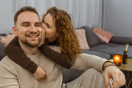 Woman whispering to smiling man while relaxing together on sofa at homeの写真素材