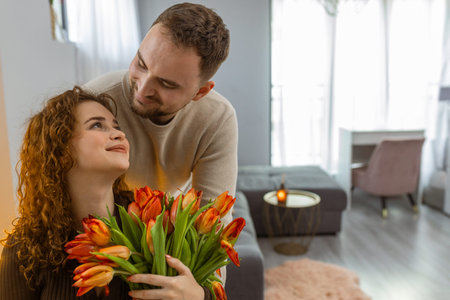 Man giving woman bouquet of tulips smiling couple celebrating love at homeの写真素材