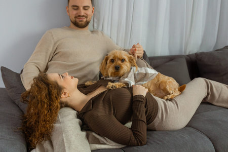 Happy couple relaxing at home with cute dog sitting on sofa in modern living roomの写真素材