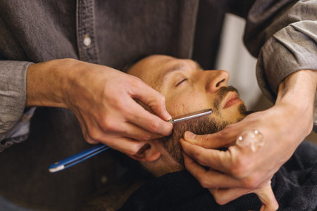 Close up of professional barber shaving male neck with straight razor in barbershop. Beard...