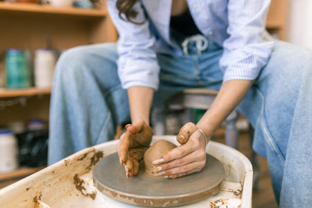 Young woman shaping clay on pottery wheel in ceramic workshop, handmade pottery process and creative...