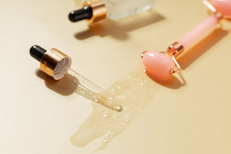 Cosmetic serum dropper and facial roller with skincare liquid texture on warm pastel background,...