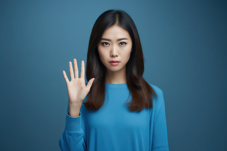 Young woman on a blue studio backdrop standing with outstretched hand showing stop sign Generative AIの素材