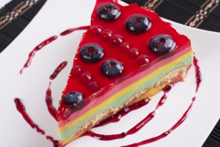 Slice of no baked cheesecake with bluberries, red currant and red jelly on the top presented on a white plateの写真素材