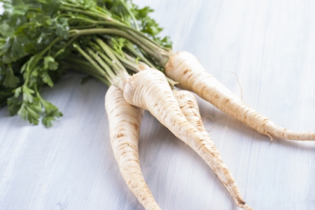 Close up photo of edible vegetables - a parsley root with some green top on a solid wooden light blue backgroundの写真素材
