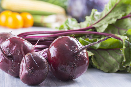 Close up photo of edible vegetables - a red beetroot with some green leafs and some vegetables in...
