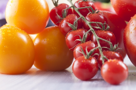 Close up photo of edible vegetables - cherry, yellow and red tomatoes on a solid light blue wooden tableの写真素材
