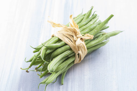 Close up photo of edible vegetables - a green bean on a solid light blue wooden table