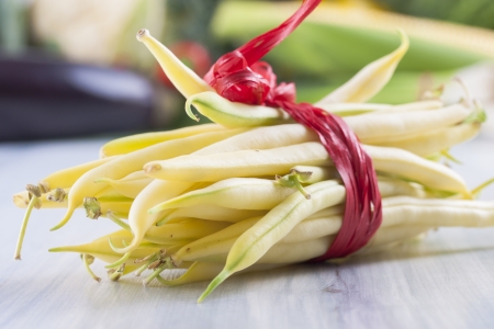 Close up photo of edible vegetables - a yellow wax bean with some vegetables in the background on a solid light blue wooden tableの写真素材