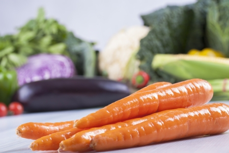 Close up photo of edible vegetables - a carrots with some vegetables in the background on a solid light blue wooden tableの写真素材