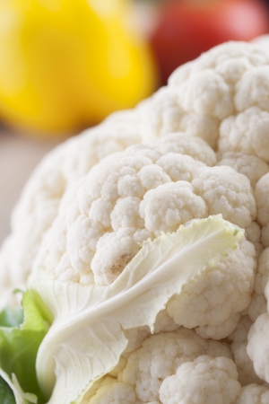 Close up photo of edible vegetables - a cauliflower with some vegetables in the background on a solid  brown wooden tableの写真素材
