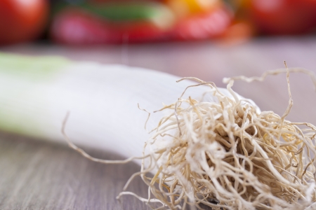 Close up photo of edible vegetables - a Leek with some vegetables in the background on a solid  brown wooden tableの写真素材