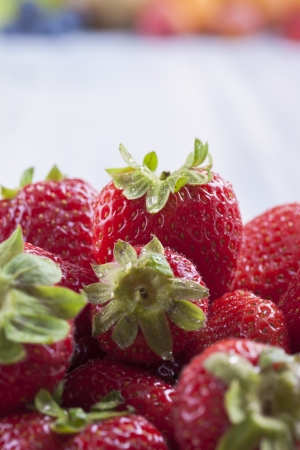 Close up photo of edible fruits - a strawberries with other full color fruits in the background on a solid  bright blue wooden tableの写真素材