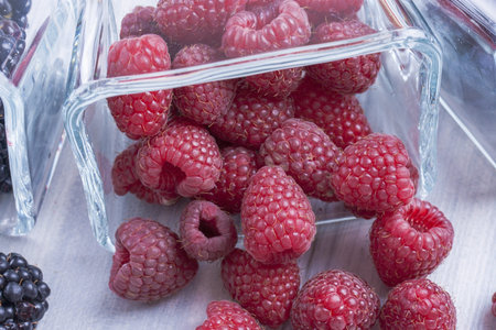 Close up photo of edible fruits - a  raspberries on a solid  bright blue wooden table