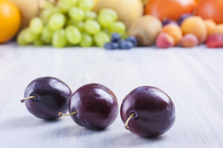 Close up photo of edible fruits - a sloes with other full colors fruits in the background on a solid  bright blue wooden tableの写真素材