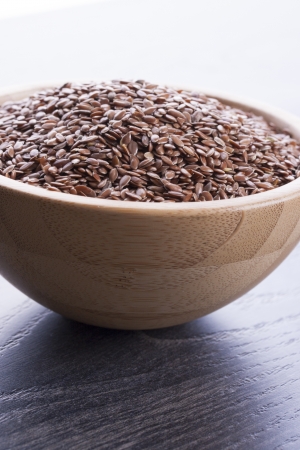 Close up photo of a raw eco food in the wooden bowl - dark brown linseeds placed on a dark wooden background.の写真素材
