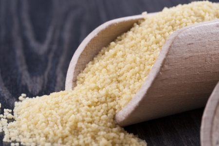 Close up photo of a raw eco food in the wooden spatulas - light yellow couscous placed on a dark wooden background.の写真素材