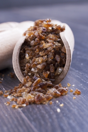 Close up photo of a food ingredients in a wooden scoop - large pieces of crystalized sugar placed on a dark wooden background.の写真素材