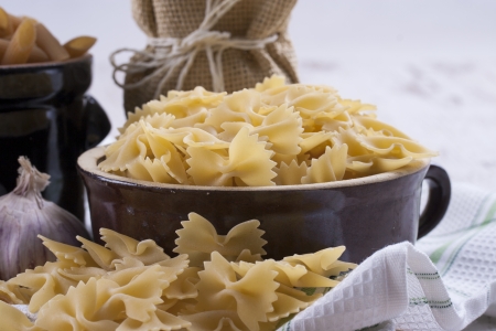 Raw food composition - yelow colored farfelle pasta in a clay pot on a bright wooden background.の写真素材