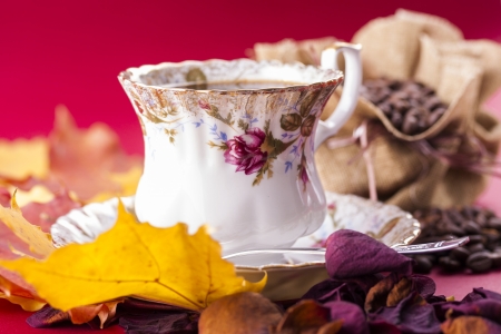 Autumn style close up photo of a hot coffee porcelain cup with the bag of the coffee beans over a red background.の写真素材