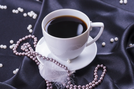 Close up photo of a hot coffee cup with pearls placed on the black satin の写真素材