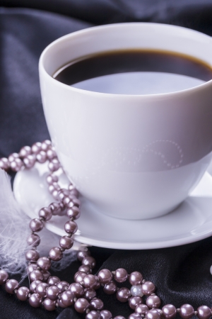 Close up photo of a hot coffee cup with pearls placed on the black satin の写真素材