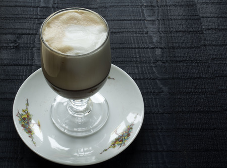 a beautifull glass with coffee latte with high foam of cream and saucer on the black backgroundの写真素材