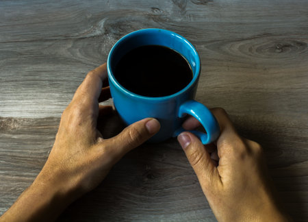 a big green coffee cup wich hold two hands on the gray wood background