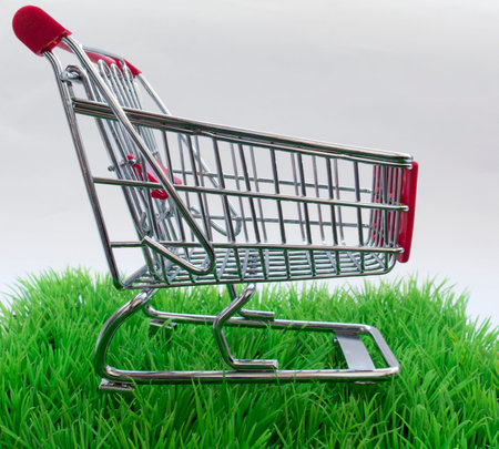 shopping trolley on a green lawn and a white background with space for textの写真素材