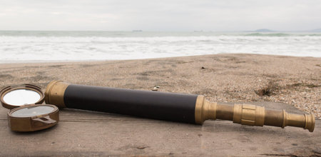 Vintage bronze compass and spyglass on the background of the sea on the sand