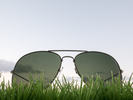 Sunglasses in the grass on blue sky backgroundの写真素材