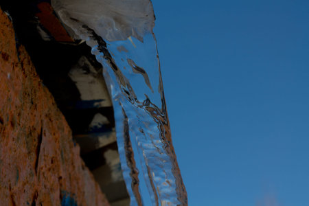 A closeup shot of a wall with icicles under the blue sky. spring is comingの写真素材