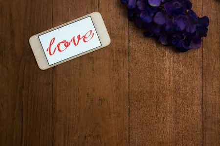 Word of love in smart phone and flower on old deskの写真素材