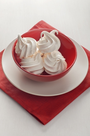 Top view of a red bowl with a lot of white meringue on a red napkin and white wooden background の写真素材