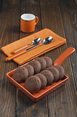 Biscuits in orange ceramic pan, mug of milk, spoons on napkin on dark wooden backgroundの写真素材
