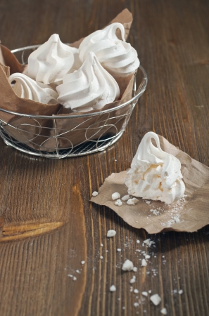 Side view of broken meringue with crumbs on paper and lot of meringues in iron bowl on dark wooden backgroundの写真素材