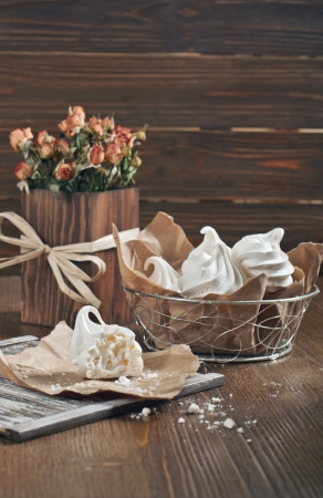 Closeup side view of broken meringue with crumbs on brown paper and lot of meringues in iron bowl on dark wooden backgroundの写真素材