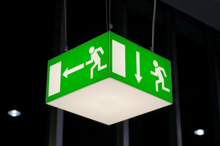 Green emergency exit sign, cube-shaped, hanging from a ceiling.の写真素材