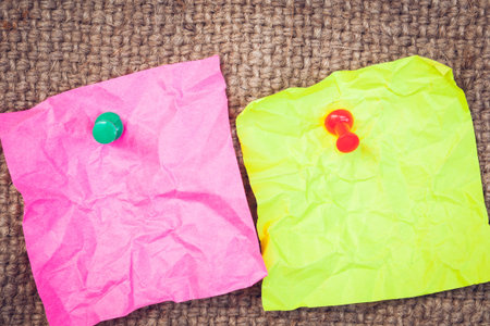Note paper pink and green with push pins on cloth sack background