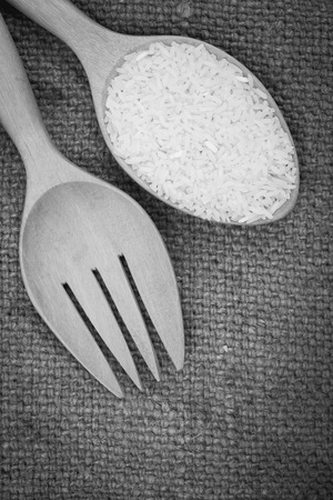 black  white image wooden fork and spoon filled with Jasmine rice on cloth sack backgroundの写真素材