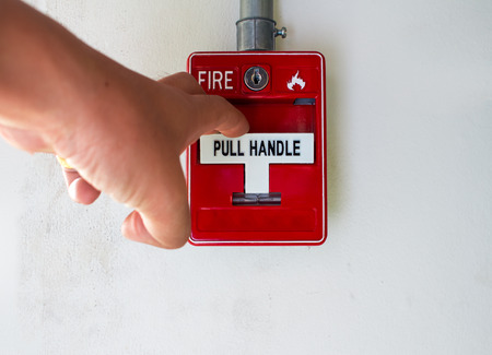 The hand of man is press fire alarm on the wall next to the doorの写真素材