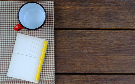 a red empty cup and fountain pen and old postcard put on fabric on wooden tableの写真素材