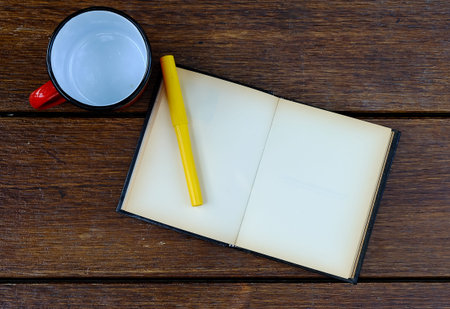 open blank old notebook on wooden table with empty red cup and yellow pen
