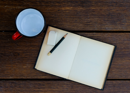open blank old notebook on wooden table with empty red cup and rubber and pencilの写真素材